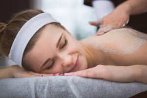 Woman lying at beautician's during exfoliating sugar scrub massage - Face and Body Institute
