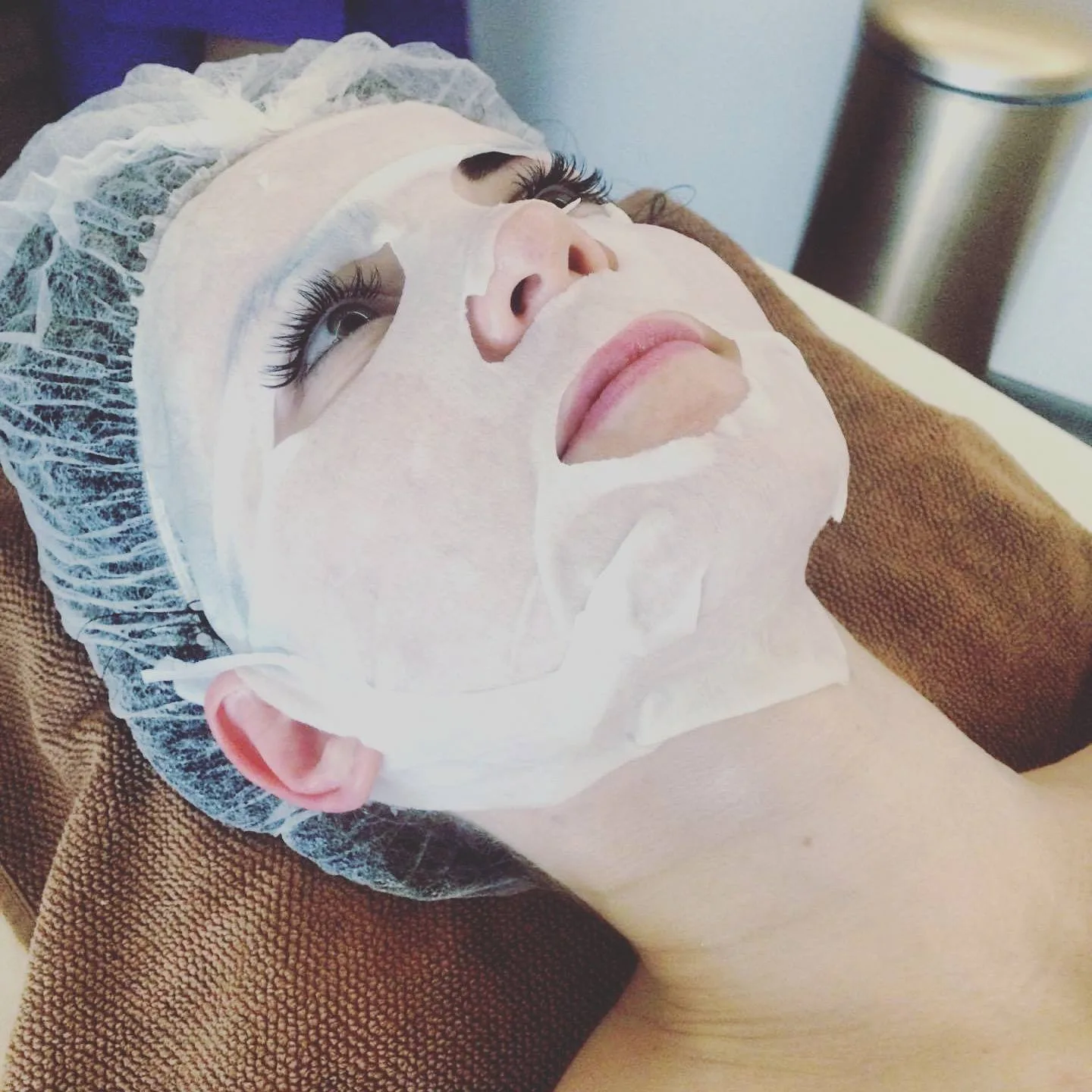Soothing sheet mask covering the face of a patient lying in a treatment cap
