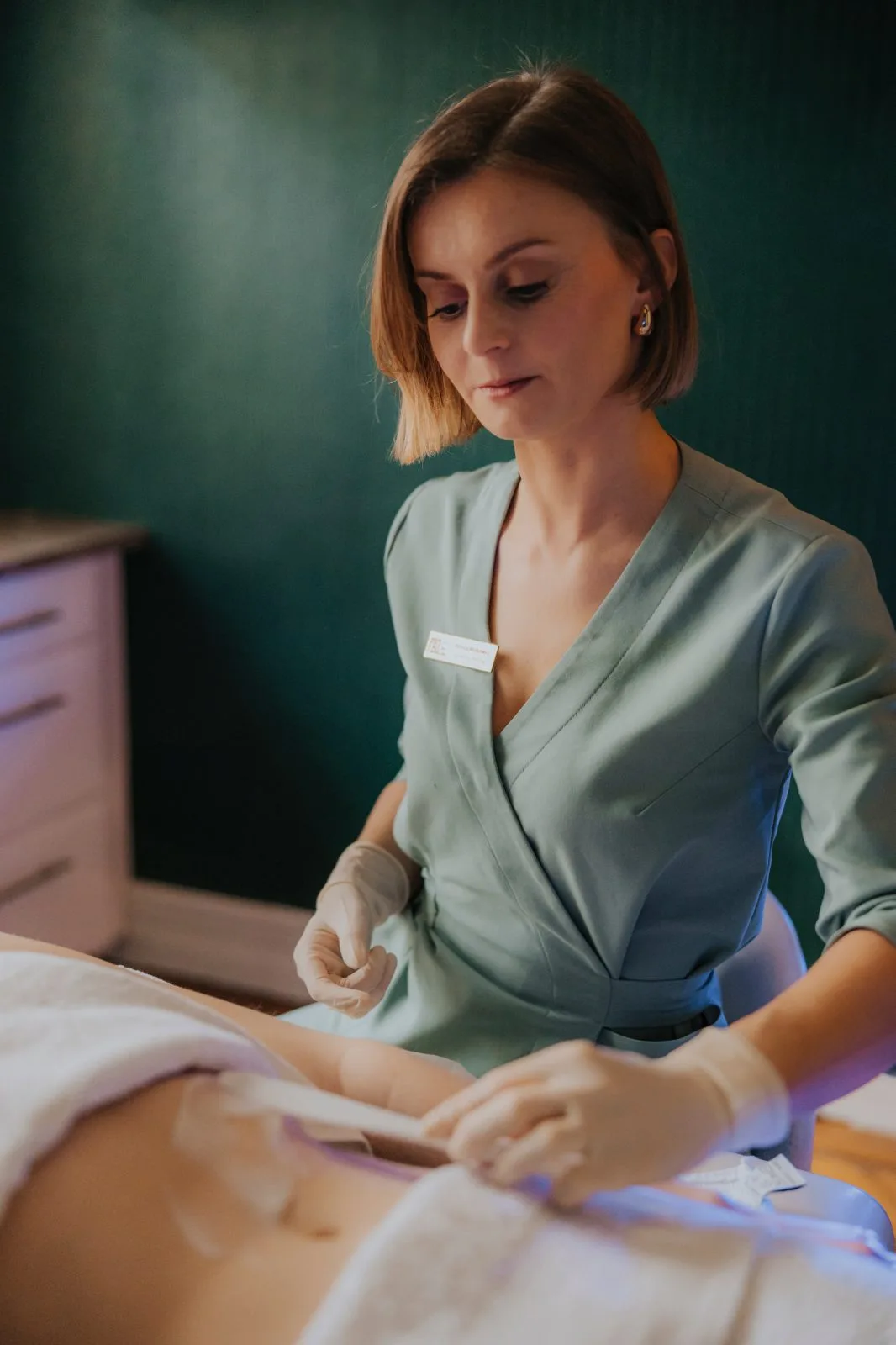 Kosmetolożka nakłada szpatułką masę do depilacji na brzuch leżącej pacjentki