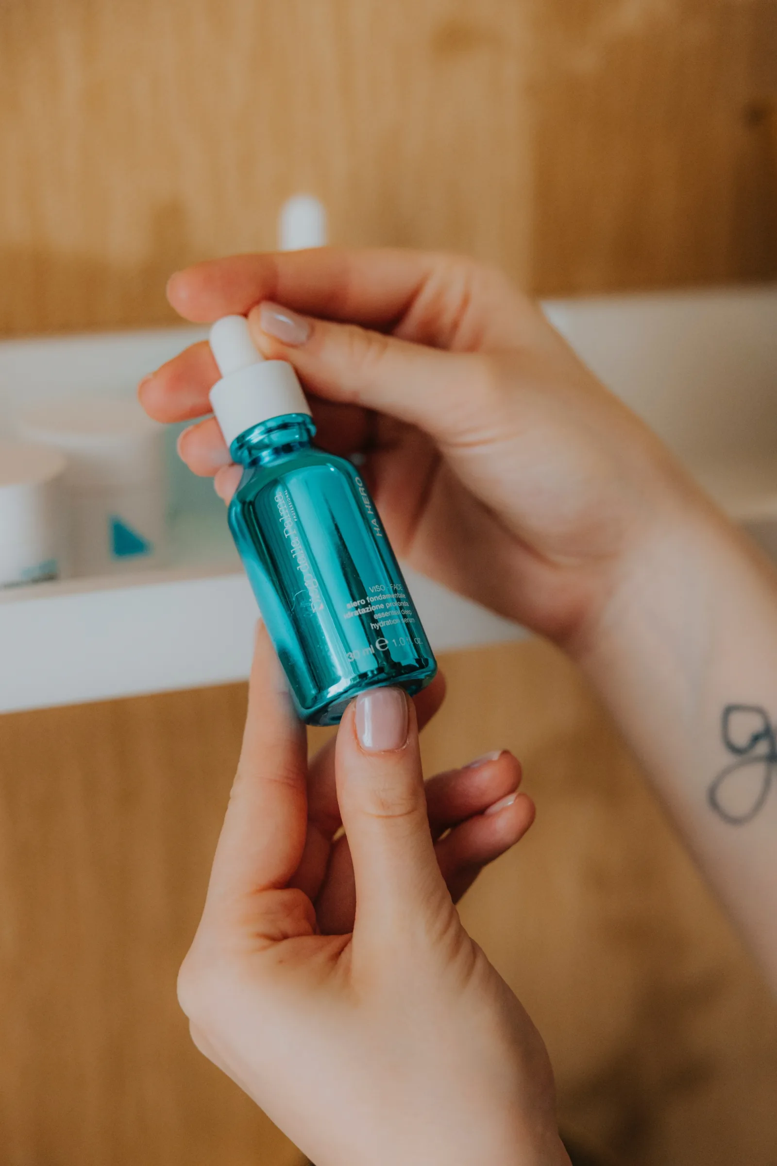 Two hands holding a turquoise dropper bottle of hyaluronic acid serum