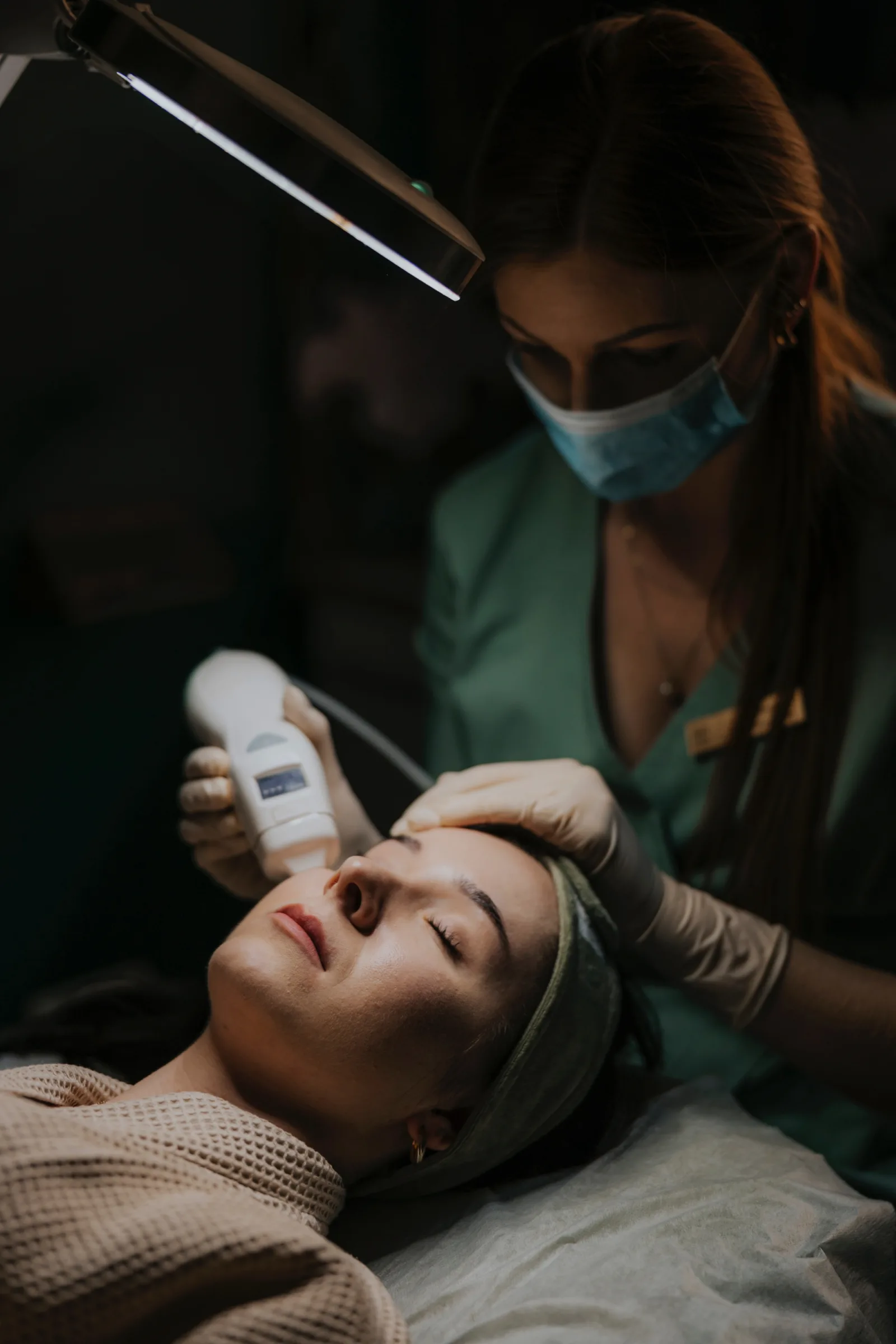 Cosmetologist moves the radiofrequency head across the forehead of a lying client