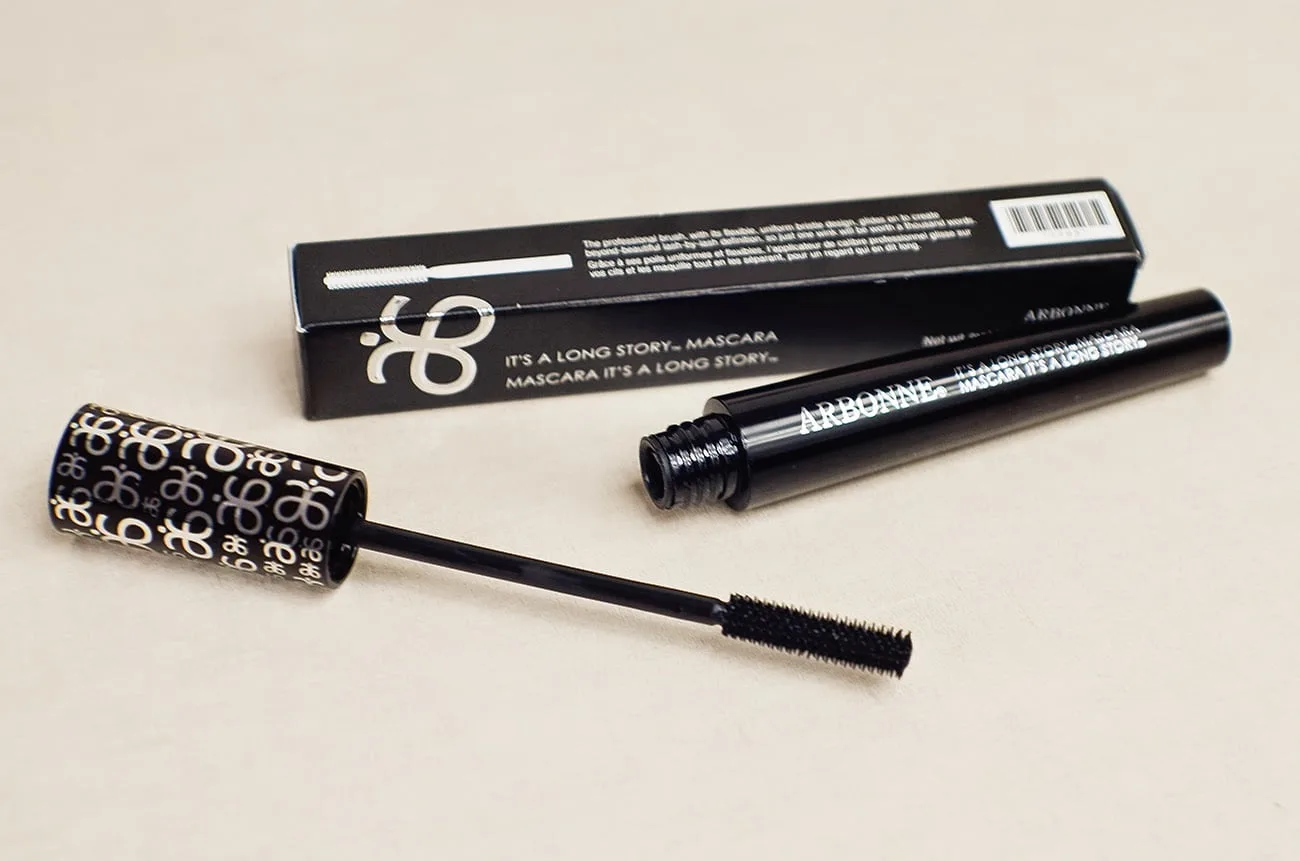 Black mascara with brush lying beside its box on a beige background